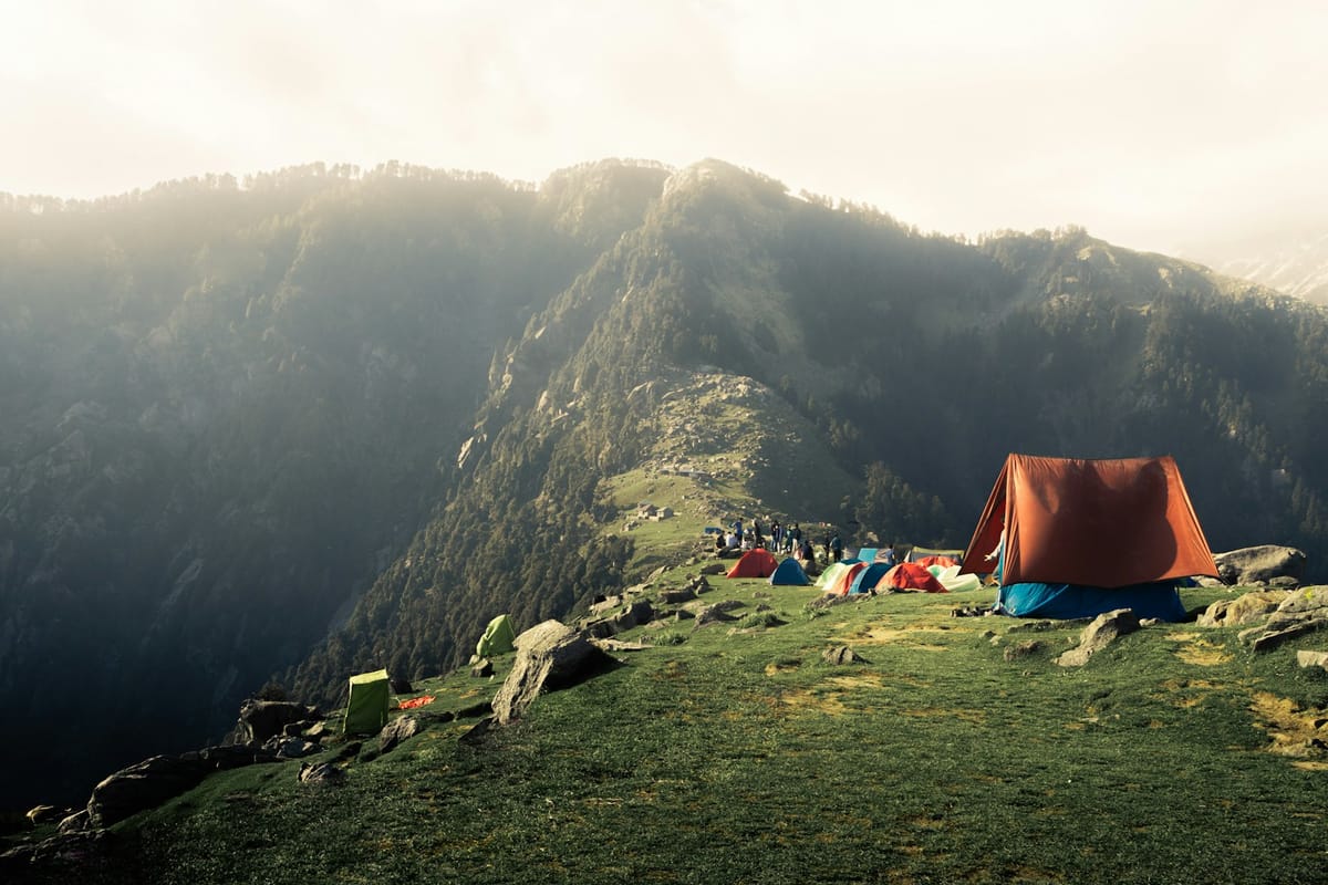 Tent pitched on a hill at dusk with mountains behind
