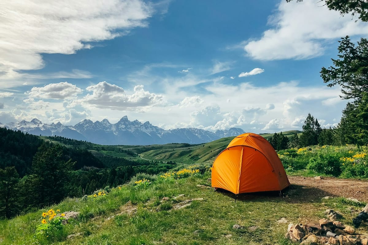 Orange dome tent on a green hillside with mountains behind